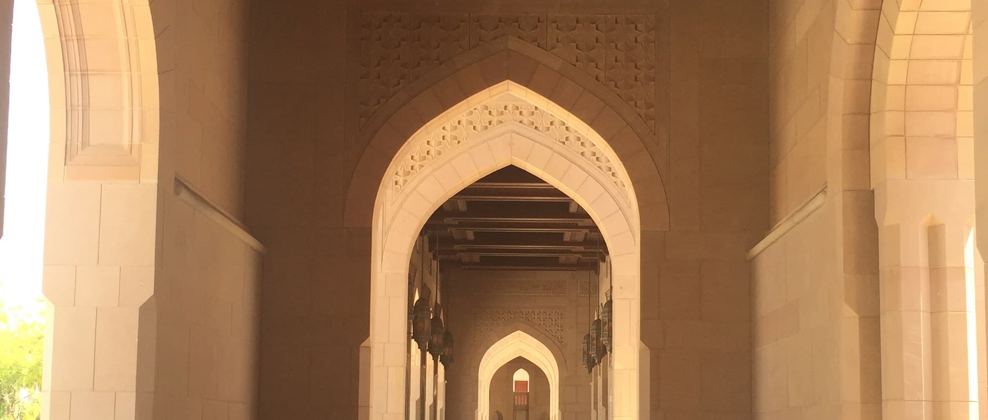 A sunlit archway inside a grand mosque, receding into a colonnade of pointed arches.