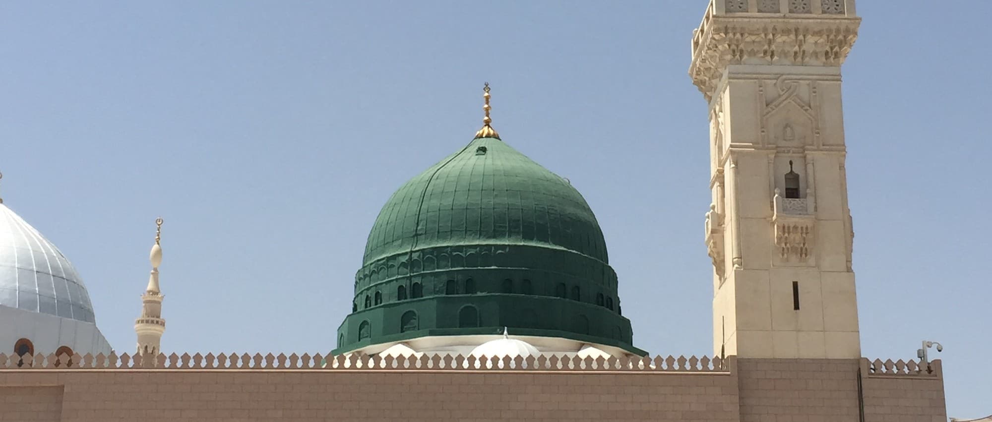 The Green Dome and a minaret of Al-Masjid an-Nabawi, the Prophet's Mosque, against a clear sky.